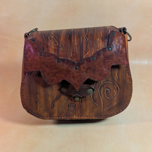 Escarcelle en cuir tanné végétal, façonnée en forme d’écorce d’arbre, avec fermoir en bois de cerf et finitions en laiton vieilli.