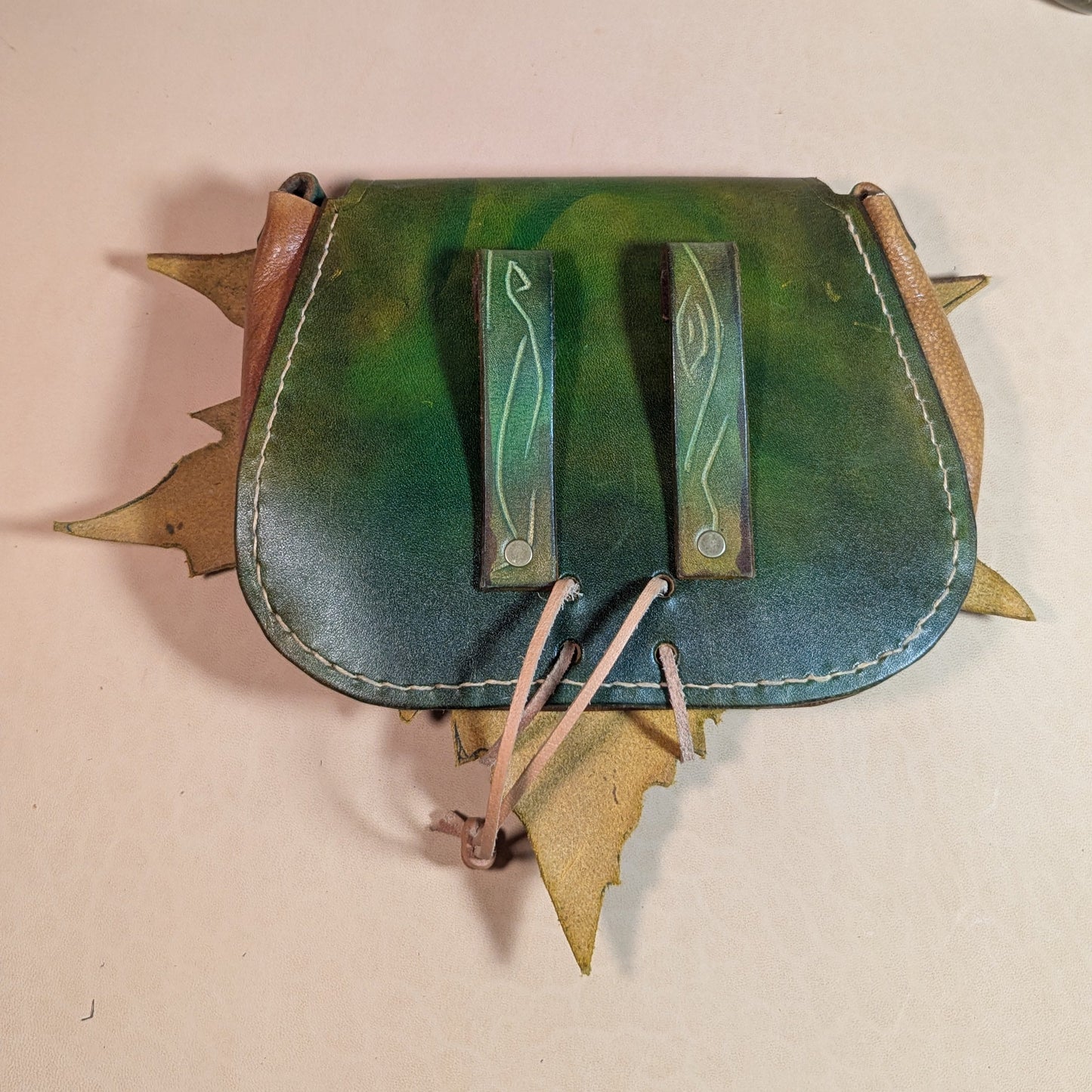 Escarcelle en cuir tanné végétal, façonnée en forme de feuille de platane, avec fermoir en bois de cerf et finitions en laiton vieilli.