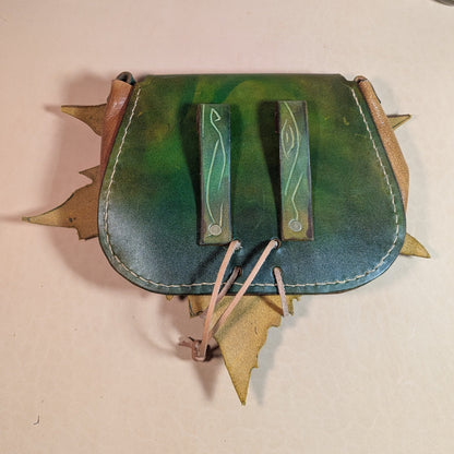 Escarcelle en cuir tanné végétal, façonnée en forme de feuille de platane, avec fermoir en bois de cerf et finitions en laiton vieilli.