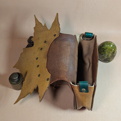 Escarcelle en cuir tanné végétal, façonnée en forme de feuille de platane, avec fermoir en bois de cerf et finitions en laiton vieilli.