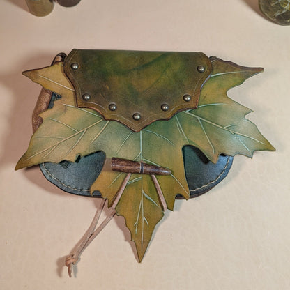 Escarcelle en cuir tanné végétal, façonnée en forme de feuille de platane, avec fermoir en bois de cerf et finitions en laiton vieilli.