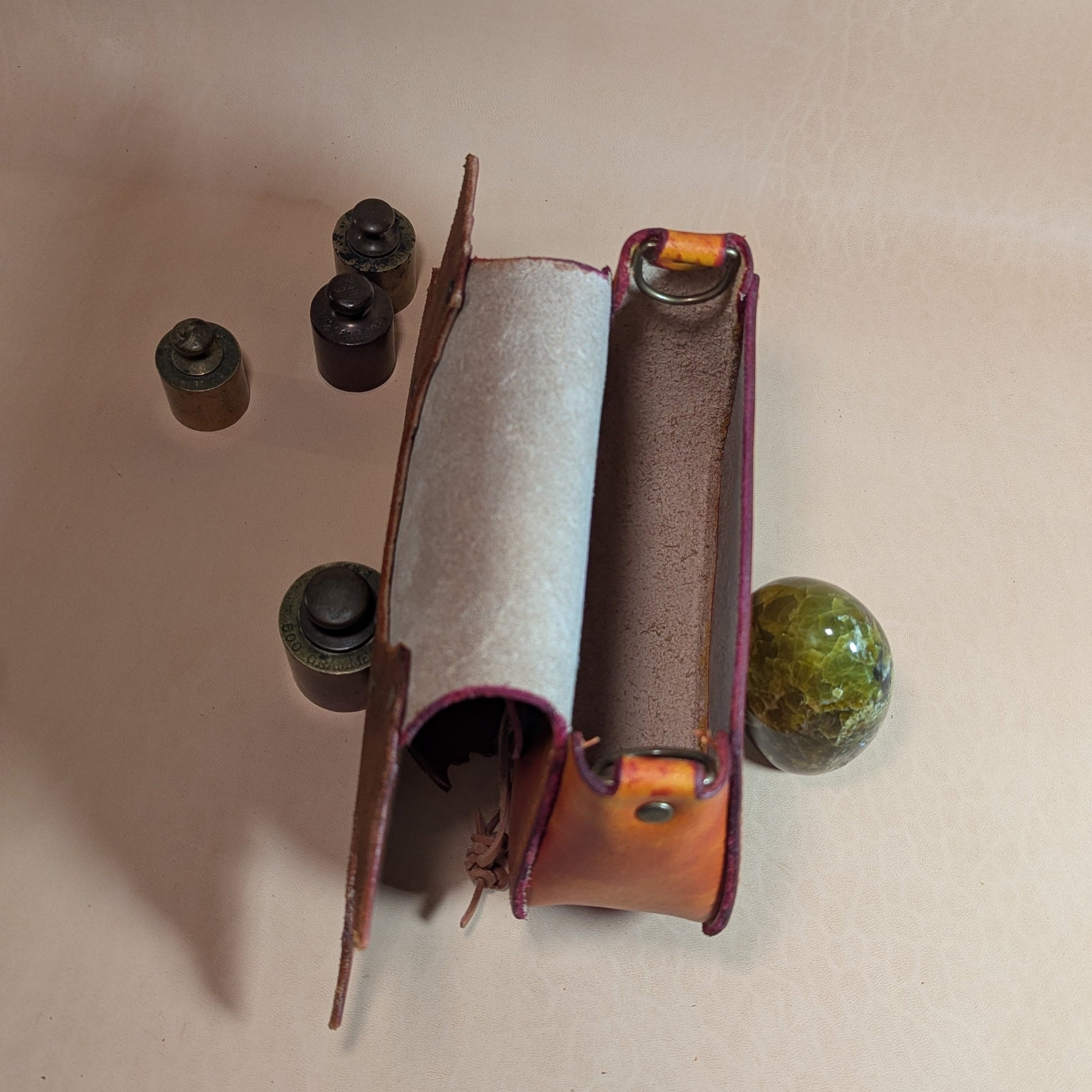 Escarcelle en cuir tanné végétal, teintée à l'alcool dans des teintes chaudes et cuivrées, avec fermoir en bois de cerf et bouclerie en laiton vieilli.